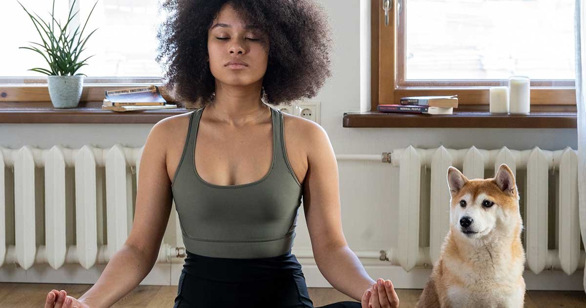A person meditating at home, eyes closed, sitting cross-legged